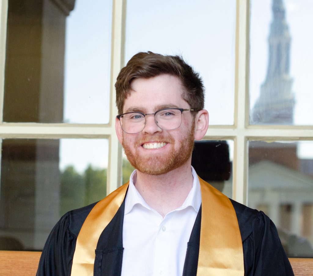 image of a person with glasses and short brown hair with a window in teh backgroundhebackground