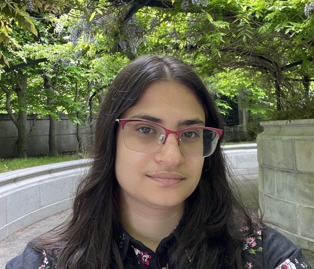 image of a person with glasses and long dark hair with green trees in the background
